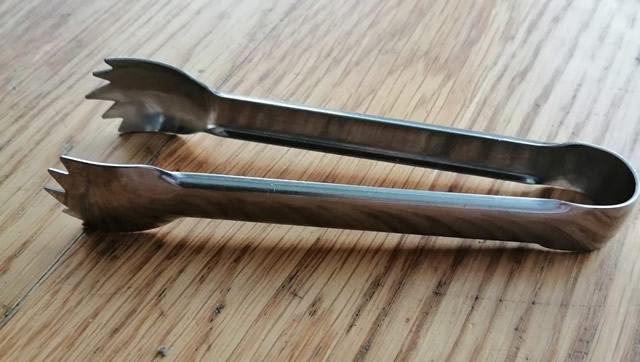 Edelstahl-Zuckerzange mit gezahnten Enden liegt auf einem Holztisch.